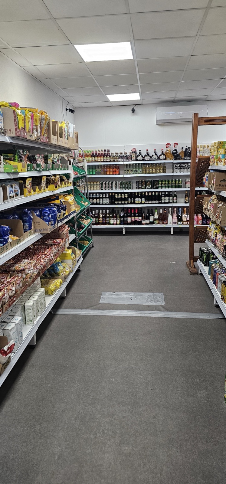 Een gangpad in de winkel met schappen vol Poolse producten en een wand met dranken